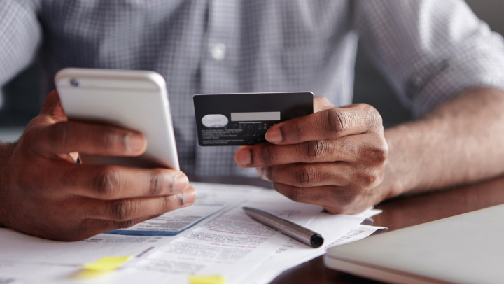 Miniaturansicht einer Person, die eine Kreditkarte und ein Telefon hält 