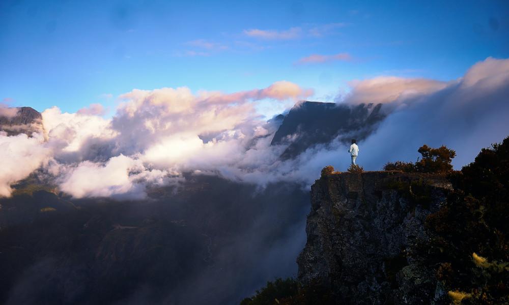 Person standing on the edge of a cliff with clouds in the background